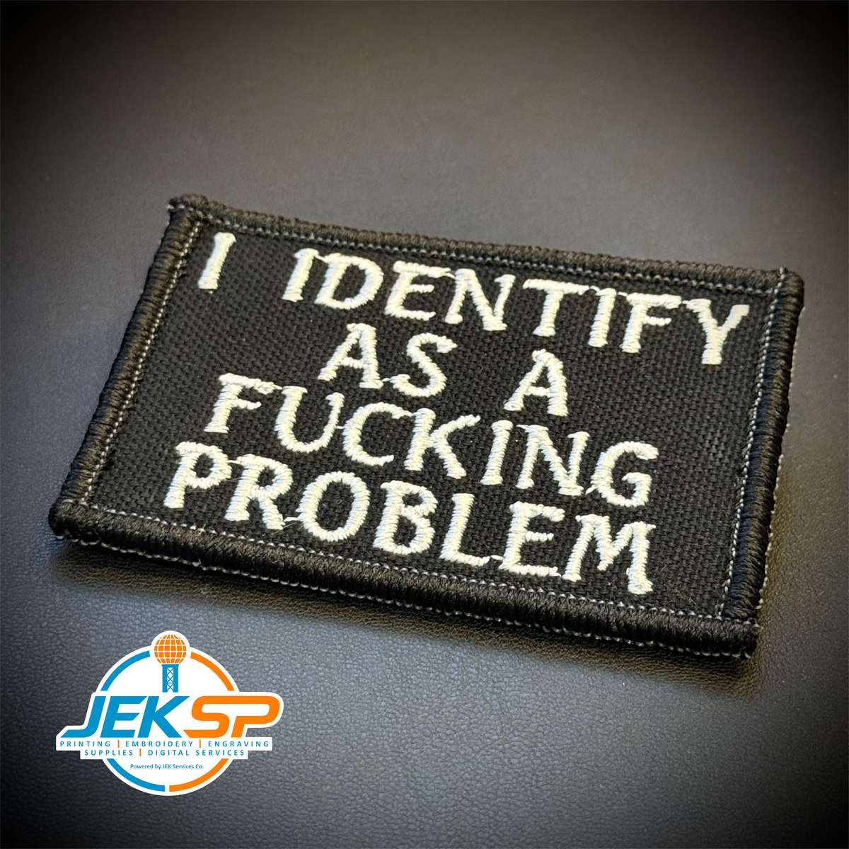 I Identify As The Problem embroidered morale patch: black embroidered patch with white text reading 'I IDENTIFY AS A FUCKING PROBLEM' on a dark textured background.