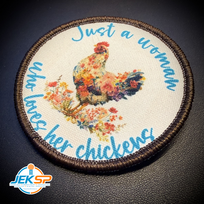 A round embroidered patch featuring a colorful floral rooster on a cream fabric background, surrounded by blue cursive text reading 'Just a woman who loves her chickens' and a dark brown stitched border. A JEKSP watermark is visible in the lower-left corner.