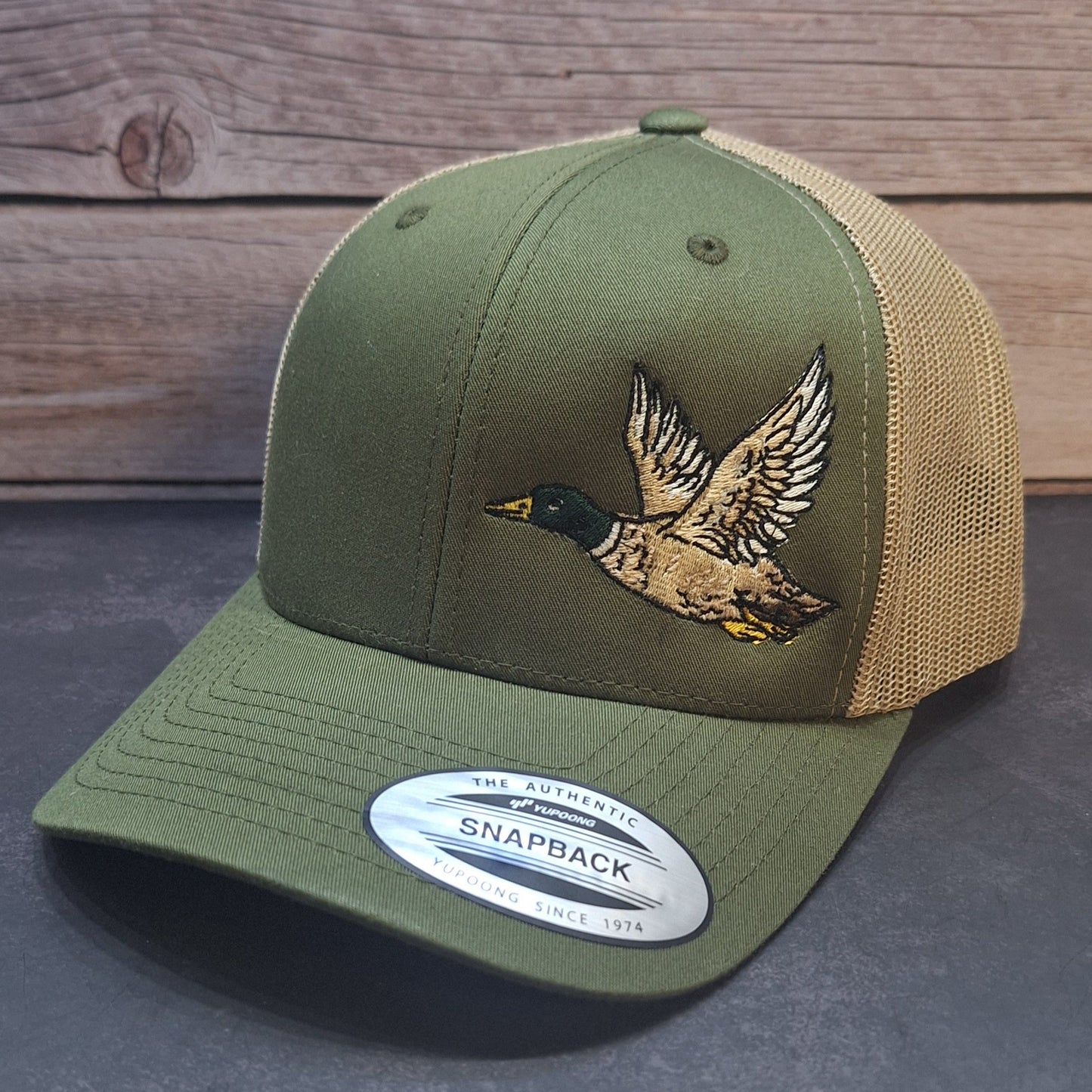 Green and beige cap with a duck design on a dark surface and wooden background