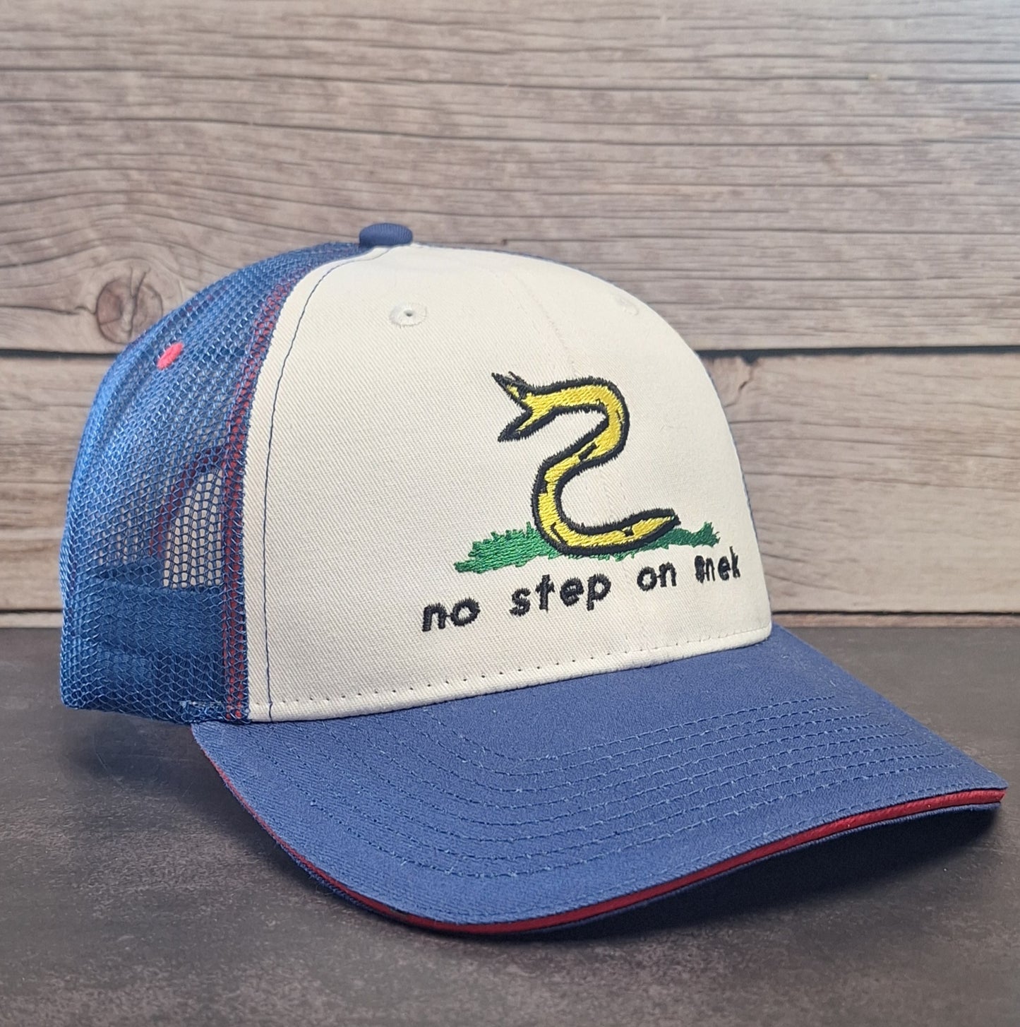 Blue and white cap with snake design and 'no step on me!' text on a wooden background