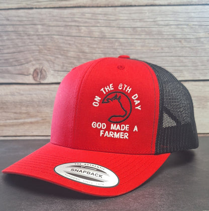 Red and black cap with text (On The 8th Day God Made A Farmer) on a wooden background