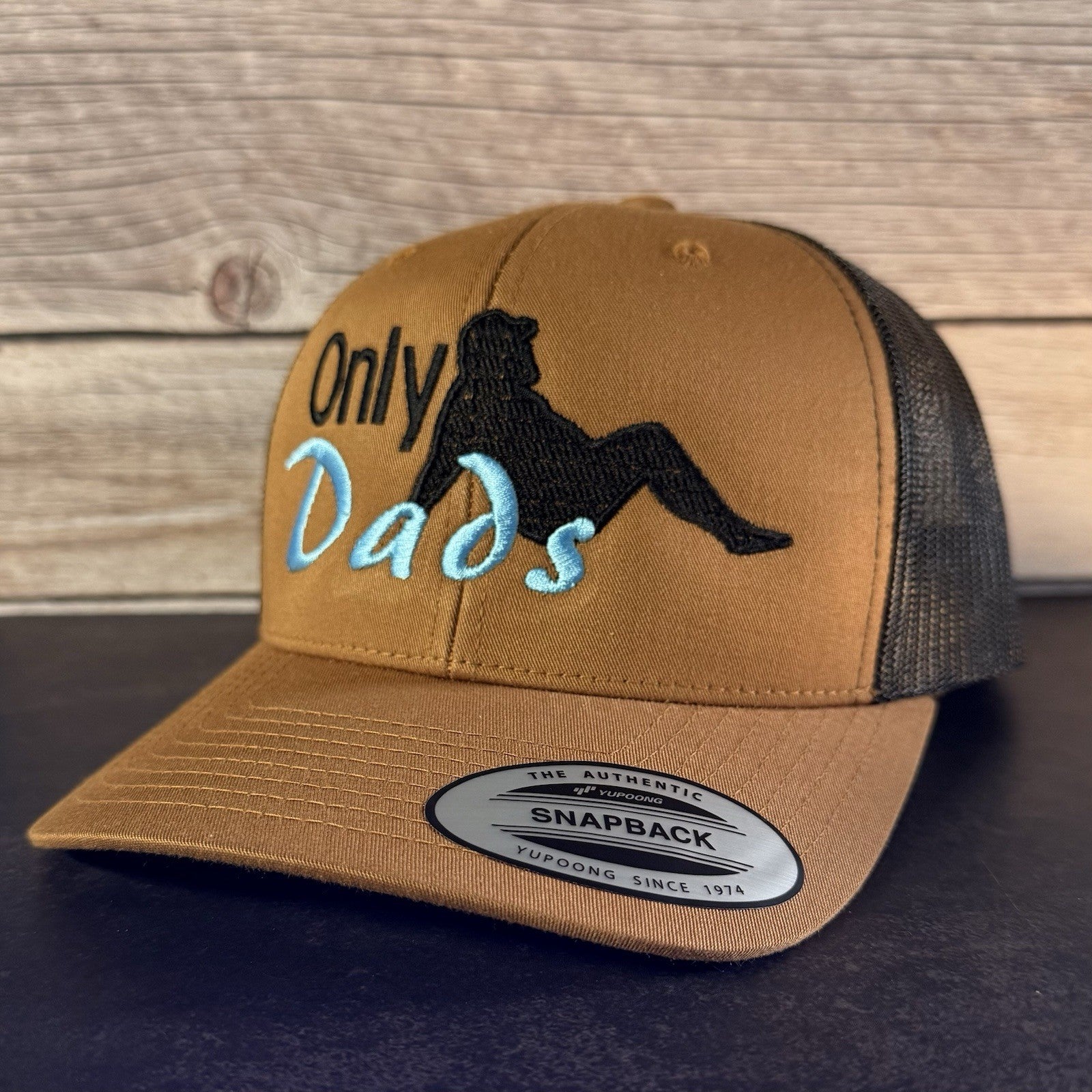 Brown cap with 'Only Dads' text and graphic on a wooden surface