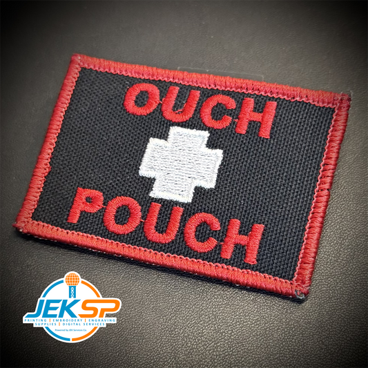 An embroidered tactical patch with a black background, red border, red text reading 'OUCH POUCH', and a white cross in the center, shown on a dark textured surface with a JEKSP watermark in the lower-left corner.