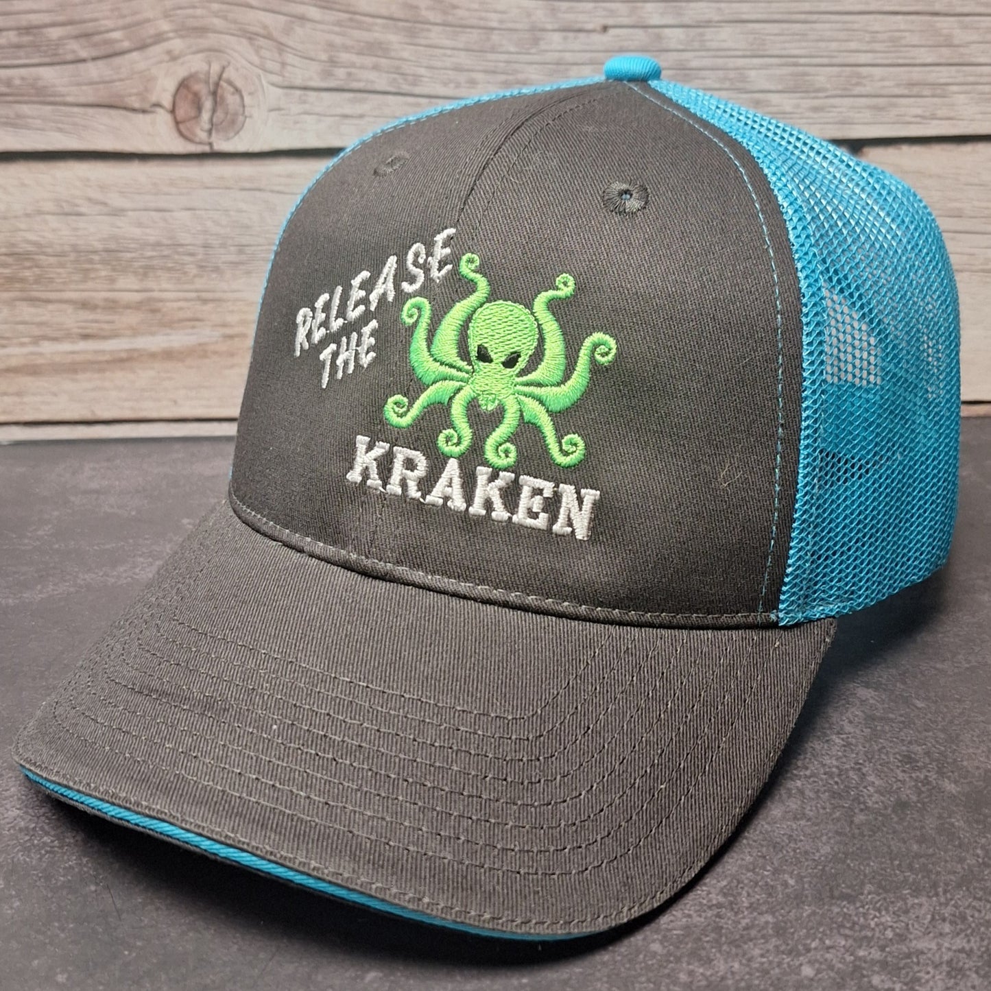 Gray and blue cap with 'Release the Kraken' text and octopus graphic on a wooden surface.