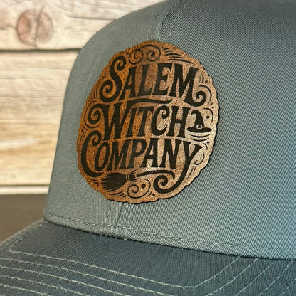Gray cap with 'Salem Witch Company' logo on a wooden surface