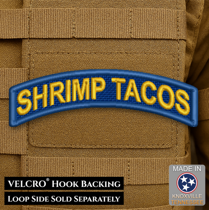 An embroidered tactical patch with the text 'SHRIMP TACOS' in yellow on a blue background, shown applied to a tan MOLLE vest. Text overlays at the bottom mention Velcro hook backing and loop side sold separately, with a 'Made in Knoxville, Tennessee' badge in the corner.