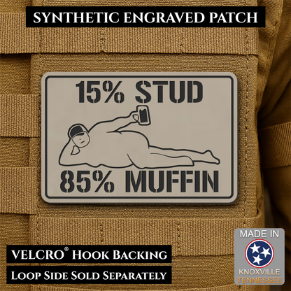 15% Stud 85% Muffin Funny Dad Bod laser-engraved synthetic morale patch: a rectangular synthetic engraved patch mounted on tan tactical MOLLE webbing. The patch is light gray with black text reading “15% STUD 85% MUFFIN” and a.