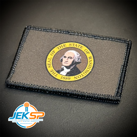 A rectangular tactical patch featuring the seal of the State of Washington, displayed on a dark textured surface. The patch has a dark gray-brown background with a black stitched border and a circular gold seal in the center.
