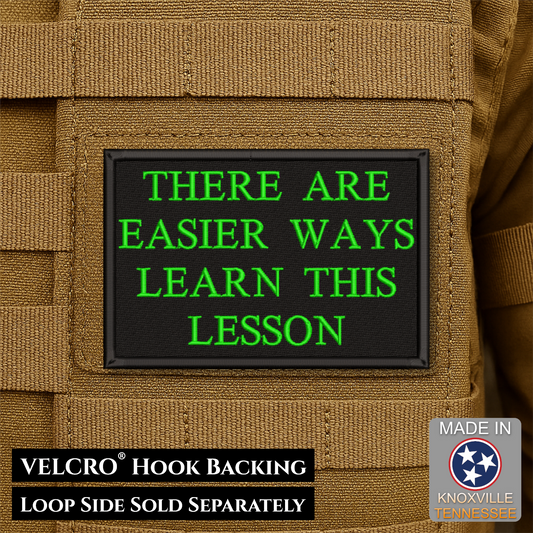 A rectangular black Velcro patch with bright green text reading 'THERE ARE EASIER WAYS LEARN THIS LESSON,' shown attached to tan tactical webbing. Text at the bottom notes 'VELCRO HOOK BACKING' and 'LOOP SIDE SOLD SEPARATELY,' with a 'Made in Knoxville Tennessee' badge in the lower right.