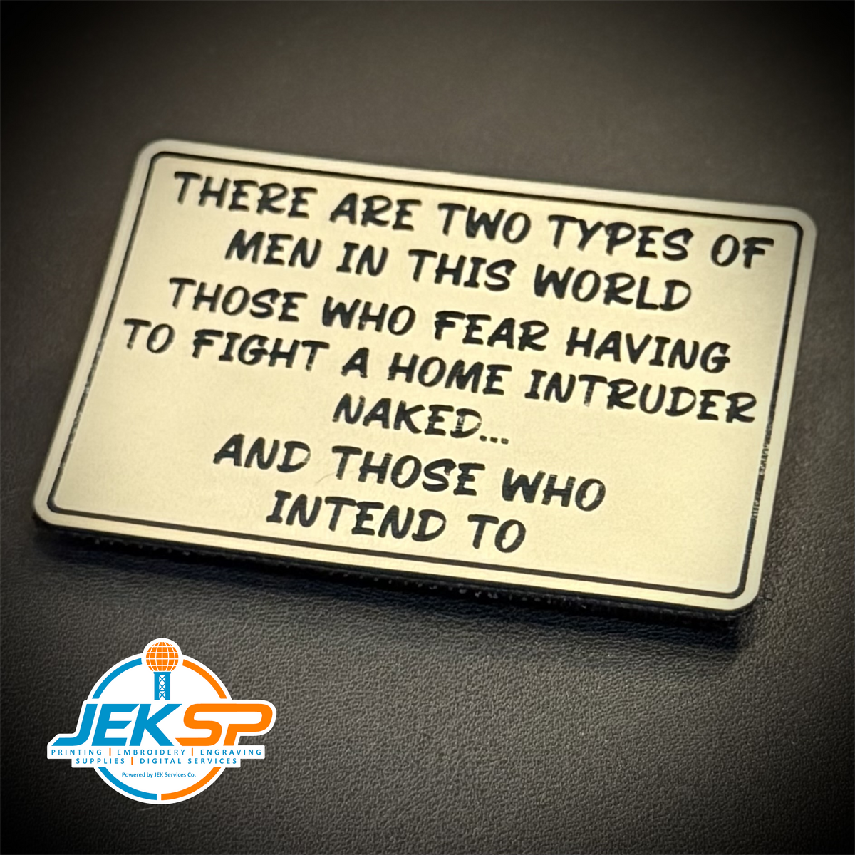 2 Types of Men In This World laser-engraved synthetic patch: a rectangular metal sign with rounded corners featuring a humorous quote about men, displayed on a dark textured surface. A logo for 'JEKSP Custom Engraving.