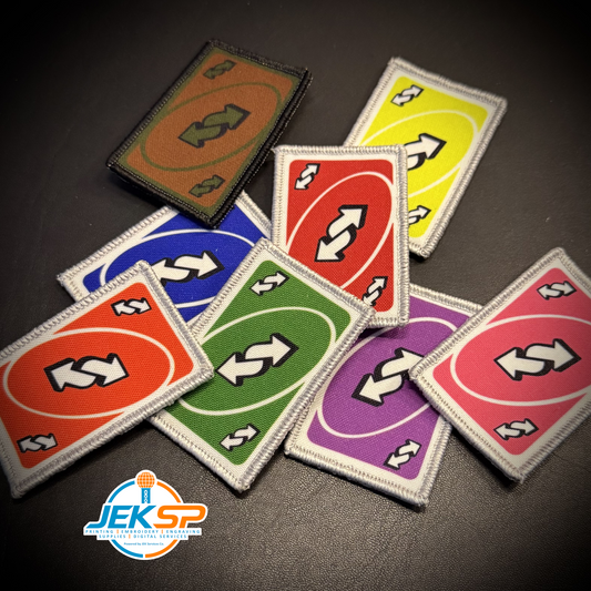 A set of embroidered rectangular patches in multiple colors, each featuring a white double-arrow symbol inside an oval on a bright background. The patches are arranged on a dark surface, with a JEKSP logo watermark in the bottom-left corner.