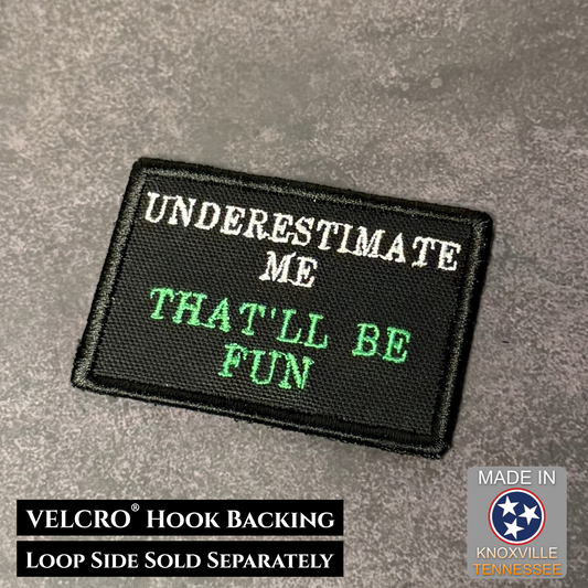 Embroidered patch with text 'UNDERESTIMATE ME THAT'LL BE FUN' on a gray background, with VELCRO hook backing information.