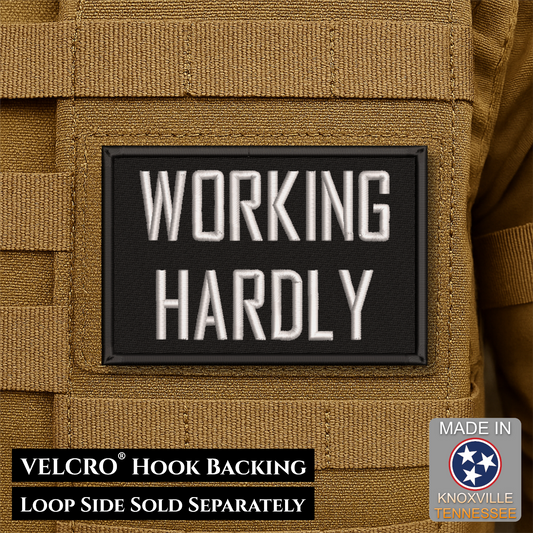 A rectangular black Velcro patch with raised white text reading 'WORKING HARDLY' mounted on tan tactical gear. Text at the bottom notes 'VELCRO HOOK BACKING' and 'LOOP SIDE SOLD SEPARATELY,' with a 'Made in Knoxville Tennessee' badge in the lower right.